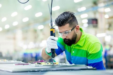 Technician in safety glasses assembling an electronic circuit board with a precision tool in a factory